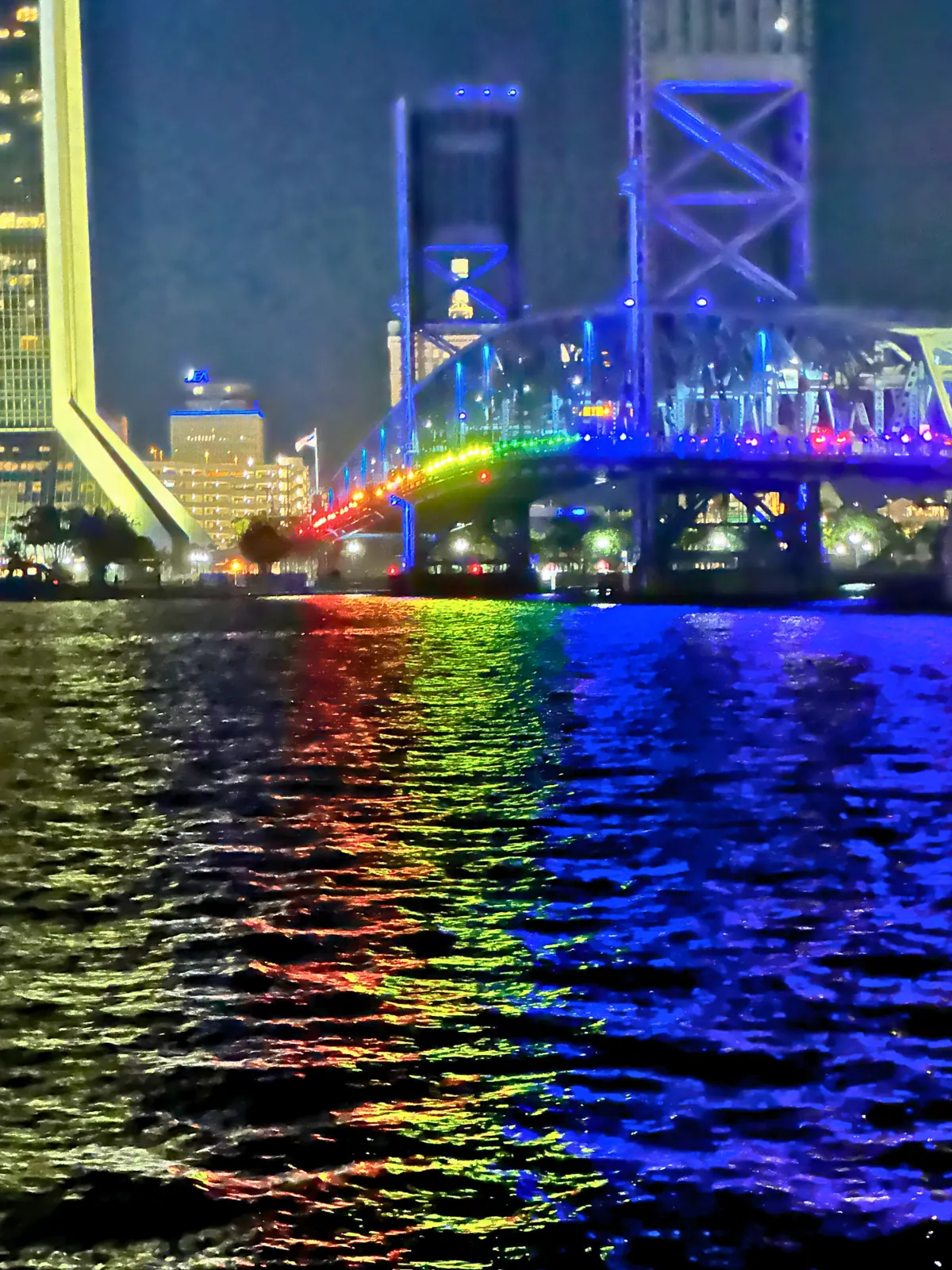 The Main Street Bridge lit in rainbow colors reflecting on the river at night